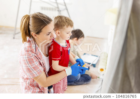 Mother with her children painting the wall with paint using roller and brush Mother with her children painting the wall with paint using roller and brush 104816765