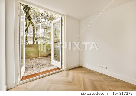 an empty room with wood flooring and large sliding glass door that opens to the backyard garden area in the background 104817272