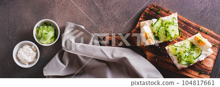 Bruschetta with ricotta, cucumber, boiled egg and sesame seeds on a board top view web banner 104817661