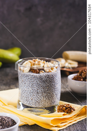 Delicious breakfast chia seeds with banana and walnuts in a glass on the table vertical view 104817684