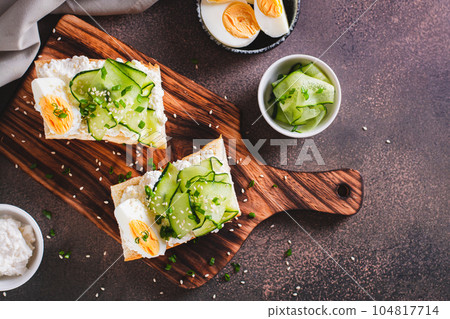 Sandwiches with ricotta, cucumber slices, boiled egg and sesame seeds on a board top view 104817714