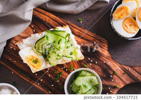 Close up of sandwich with ricotta, cucumber slices, boiled egg and sesame seeds on a board top view 104817715