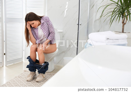 Woman suffering from hemorrhoid on toilet bowl in rest room 104817732