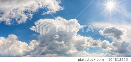 Bright sun shines high in a blue summer sky panorama. 104818223