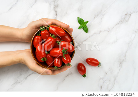 Bowl of fresh Ornela cherry tomatoes in a woman hands over white marble background. Bowl of fresh Ornela cherry tomatoes in a woman hands over white marble background. 104818224