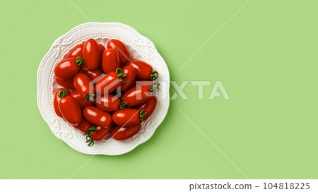 Red Ornela cherry tomatoes on a white plate over green background. Red Ornela cherry tomatoes on a white plate over green background. 104818225