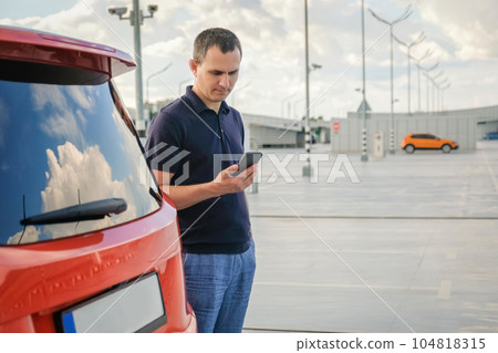 A man stands near his car in the parking lot and uses the phone A man stands near his car in the parking lot and uses the phone 104818315
