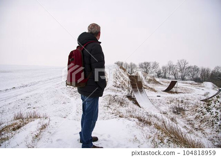 Middle age man standing in beautiful winter landscape . Man viewing on abandoned freestyle motocross ramps Middle age man standing in beautiful winter landscape . Man viewing on abandoned freestyle motocross ramps 104818959