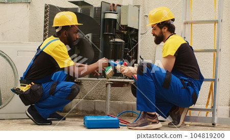 Efficient technicians assembling professional pressure manifold gauges to check liquids and gases in hvac system while seasoned mechanic cleans layer of built up dirt and dust in air conditioner Efficient technicians assembling professional pressure manifold gauges to check liquids and gases in hvac system while seasoned mechanic cleans layer of built up dirt and dust in air conditioner 104819200