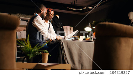 Tailors preparing fabric pattern for fashion collection manufacturing process, choosing perfect design on sketches. Couturier and assistant working on clothing line creation. Tripod shot. Tailors preparing fabric pattern for fashion collection manufacturing process, choosing perfect design on sketches. Couturier and assistant working on clothing line creation. Tripod shot. 104819237