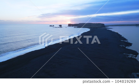 Aerial view of black sand beach with mountains and big stones in iceland, beautiful natural scenery on reynisfjara beach. Icelandic landscape with atlantic ocean on coastline. Slow motion. Aerial view of black sand beach with mountains and big stones in iceland, beautiful natural scenery on reynisfjara beach. Icelandic landscape with atlantic ocean on coastline. Slow motion. 104819269