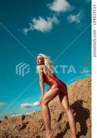 Beautiful blond woman in a red sexy dress on the background of the sky and sand. Beautiful blond woman in a red sexy dress on the background of the sky and sand. 104819314