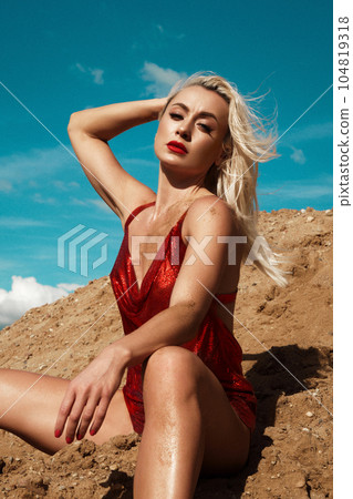 Beautiful blond woman in a red sexy dress on the background of the sky and sand. 104819318