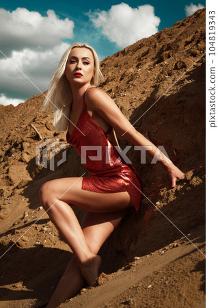 Beautiful blond woman in a red sexy dress on the background of the sky and sand. Beautiful blond woman in a red sexy dress on the background of the sky and sand. 104819343