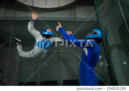 A male instructor teaches a woman how to fly in a wind tunnel. Free fall simulator. 104820180