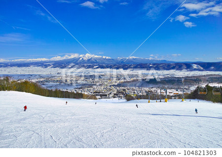 陽光明媚的日子，從富良野滑雪場眺望十勝嶽山脈，滑雪者們在北之峰地區廣闊的初級滑雪道上滑雪 104821303