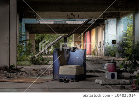 The old blue upholstered chair is in the middle of the abandoned buildings, it was left over years. 104823014
