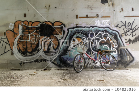 A red bicycle is parked beside the graffiti patterns on the wall. A red bicycle is parked beside the graffiti patterns on the wall. 104823016