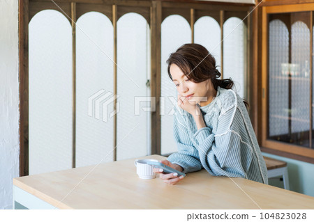 照片:一位穿著針織衫的女士看著智能手機 照片:一位穿著針織衫的女士看著智能手機 104823028