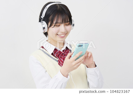 A high school girl wearing headphones and listening to music on her smartphone White background 104823167