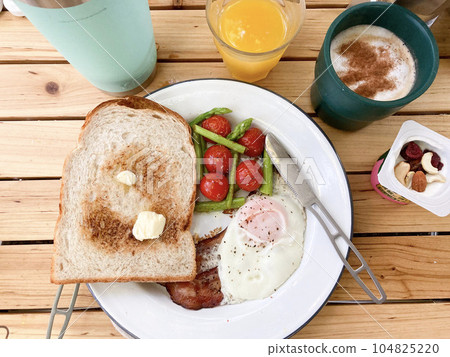 Cappuccino with cinnamon on a white plate with toast, bacon eggs and tomatoes on a wooden table 104825220