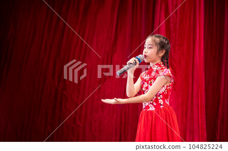 The Asian kid girl sing a song on stage at her school activity day, dress in Qipao style, red curtain background 104825224