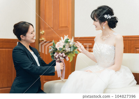 A wedding planner woman in a suit working at a wedding hall / hotel giving a bouquet to the bride 104827396