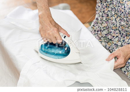 Senior woman ironing a white cutter shirt Senior woman ironing a white cutter shirt 104828811
