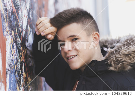Portrait of teenager leaning against a wall in the street, looking at the camera. 104829613