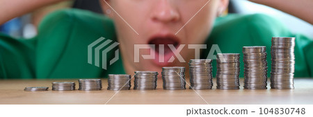 Shocked and surprised woman looks at stacks of coins on table. Shocked and surprised woman looks at stacks of coins on table. 104830748