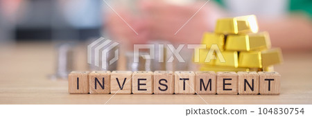 Word investment with gold bars and stacks of coins on table. Word investment with gold bars and stacks of coins on table. 104830754