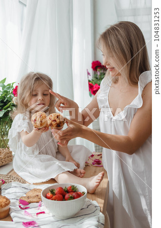 A little blonde girl with her mom on a kitchen countertop decorated with peonies. The concept of the relationship between mother and daughter. Spring atmosphere. A little blonde girl with her mom on a kitchen countertop decorated with peonies. The concept of the relationship between mother and daughter. Spring atmosphere. 104831253