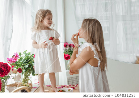 A little blonde girl with her mom on a kitchen countertop decorated with peonies. The concept of the relationship between mother and daughter. Spring atmosphere. A little blonde girl with her mom on a kitchen countertop decorated with peonies. The concept of the relationship between mother and daughter. Spring atmosphere. 104831255