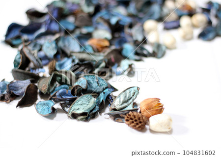 A mix of dry flowers, leaves, petals, and other plant parts. Potpourri background. Purple and blue tone leaves, white color and wood grain background shot. 104831602