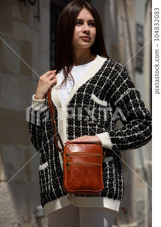 photo of beautiful woman in a white leggings, T-shirt and sweater posing with small brown leather bag photo of beautiful woman in a white leggings, T-shirt and sweater posing with small brown leather bag 104832083