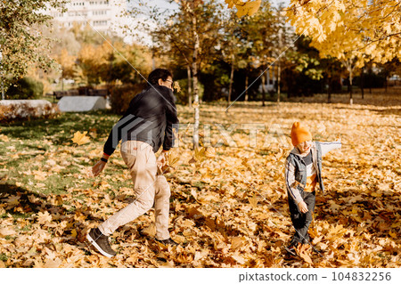 Father and son having fun in autumn park with fallen leaves, throwing up leaf. Child kid boy and his dad outdoors playing with maple leaves. 104832256