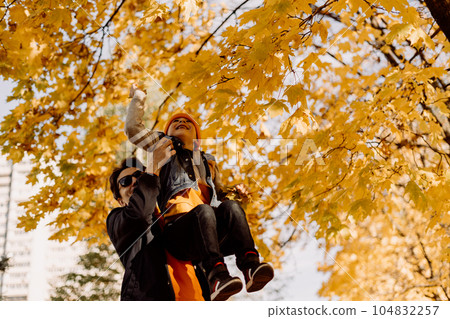 Father and son having fun in autumn park with fallen leaves, throwing up leaf. Child kid boy and his dad outdoors playing with maple leaves. 104832257