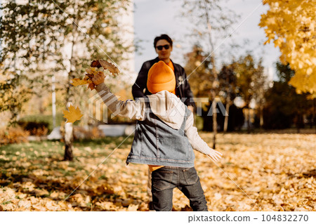 Father and son having fun in autumn park with fallen leaves, throwing up leaf. Child kid boy and his dad outdoors playing with maple leaves. 104832270