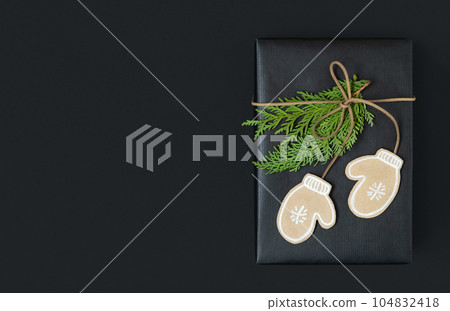 Black craft gift box with paper mittens and cedar tree branches on dark background with space for your text Black craft gift box with paper mittens and cedar tree branches on dark background with space for your text 104832418