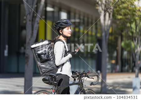 一個送餐的女人,手裡拿著智能手機,拉著一輛公路自行車 一個送餐的女人,手裡拿著智能手機,拉著一輛公路自行車 104834531