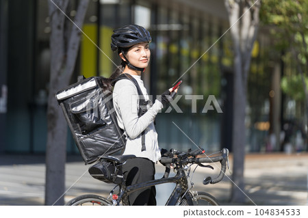 一個送餐的女人,手裡拿著智能手機,拉著一輛公路自行車 一個送餐的女人,手裡拿著智能手機,拉著一輛公路自行車 104834533