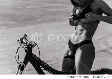 Caucasian woman in underwear posing with a bike on a hot summer day. A girl with a perfect flat stomach. Monochrome.  104834785