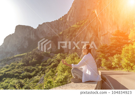 Yoga woman mountains. Profile of a woman doing yoga in the top of a cliff in the mountain. Woman meditates in yoga asana Padmasana 104834923
