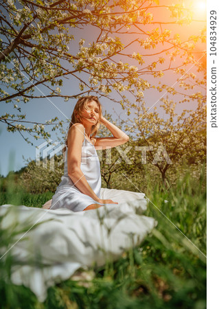 woman sleeps on a white bed in the fresh spring grass in the garden. Dressed in a blue nightgown. woman sleeps on a white bed in the fresh spring grass in the garden. Dressed in a blue nightgown. 104834929