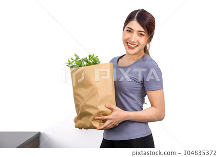 Young asian woman in casual wear stand with a smile, holding paper bag full with vegetable. 104835372