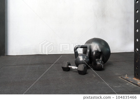 A sturdy iron kettlebell and a set of dumbbells are on the gym floor. Their robust metal bodies are glistening from recent use, highlighting the expectation of a rigorous workout routine. 104835466