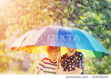 Boy and girl standing outdoors in rainy day under colourful umbrella. Boy and girl standing outdoors in rainy day under colourful umbrella. 104836262