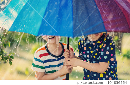 Boy and girl standing outdoors in rainy day under colourful umbrella. Boy and girl standing outdoors in rainy day under colourful umbrella. 104836264