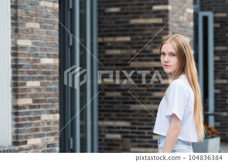 young woman enters the door of a city building against a blurred urban background 104836384