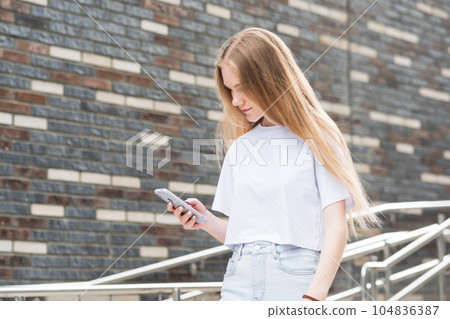 young woman with a phone against a blurred urban background young woman with a phone against a blurred urban background 104836387